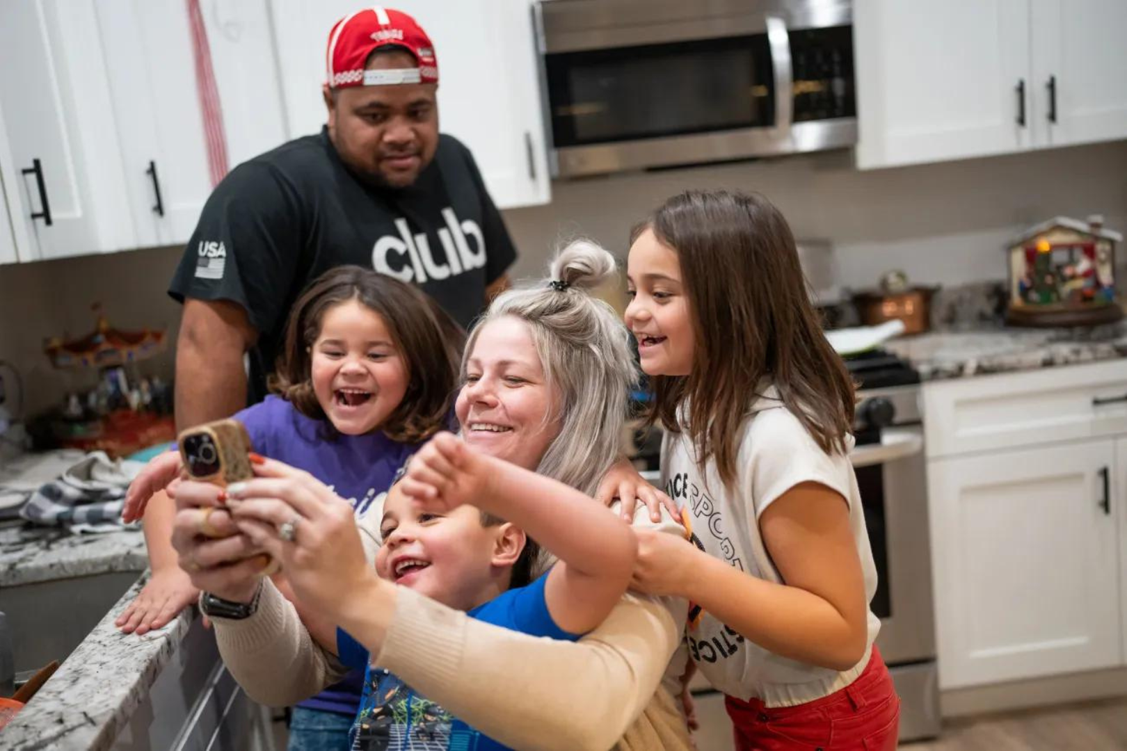 Maka Palu, back, looks on as his wife, Jessica Palu, and three of their children, Lini, 5; Bubba, 4; and Fine, 7, look at a video on her phone at their home in Eagle Mountain on Tuesday, Nov. 28, 2023.