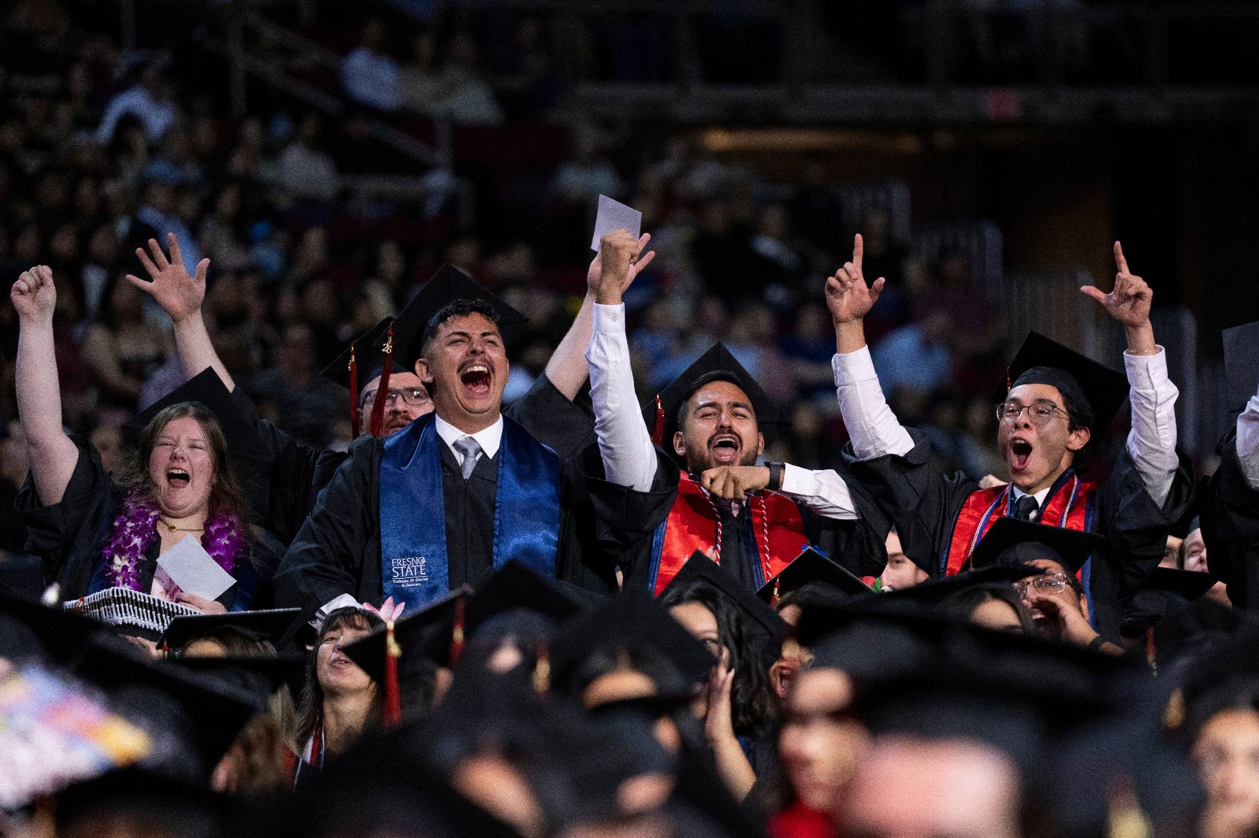 A group of males and female standing and cheering with their hands up during the event