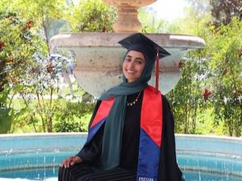 Camalah Saleh siting in graduation robe in front of fountain